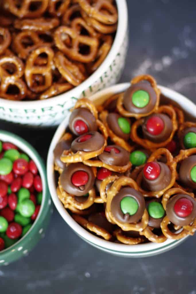 M&M pretzel kiss treats in a bowl next to a bowl of plain pretzels and red and green M&Ms