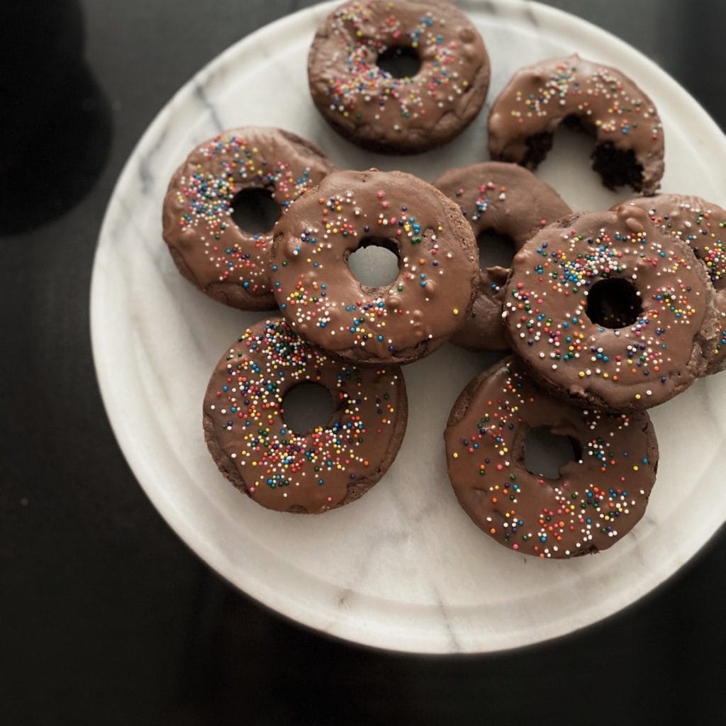 Chocolate donuts with colorful sprinkles on a white plate, perfect for bakery treats and breakfast.