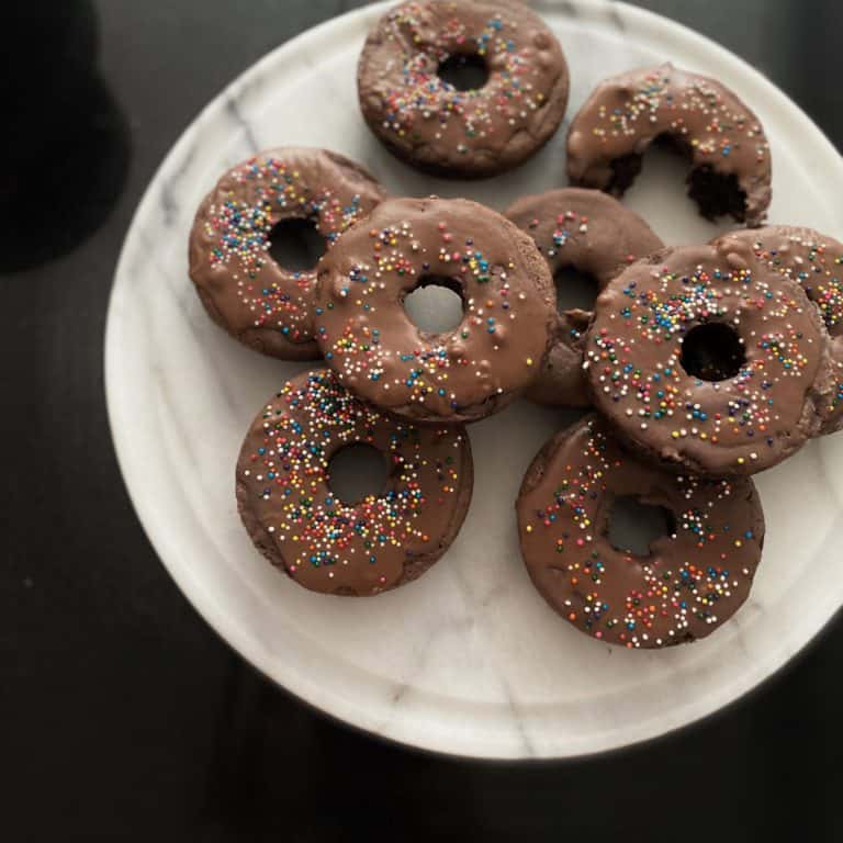 Chocolate donuts with colorful sprinkles on a white plate, perfect for bakery treats and breakfast.