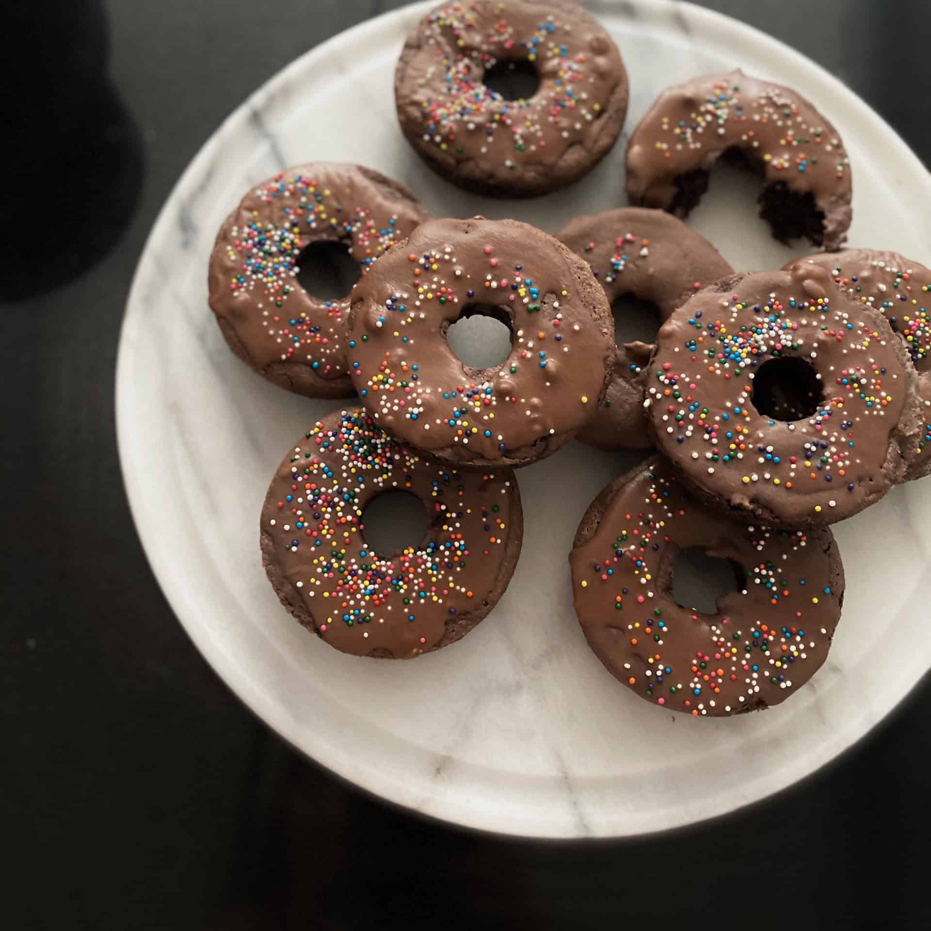 Chocolate donuts with colorful sprinkles on a white plate, perfect for bakery treats and breakfast.