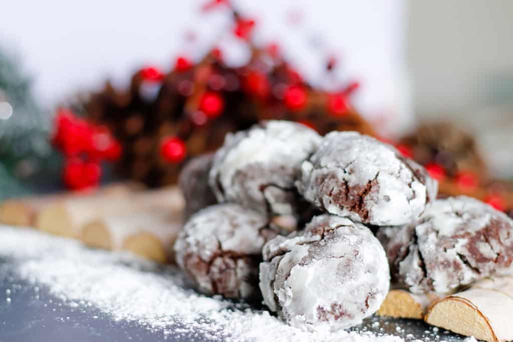 Fudgy chocolate snowball cookies on festive holiday table with powdered sugar, Christmas decorations, and red berries, perfect for holiday baking and dessert recipes.