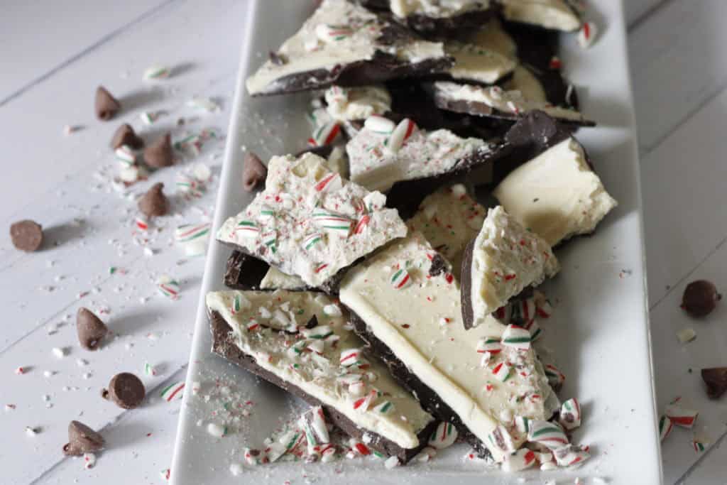 Chocolate peppermint bark with crushed candy canes and mini chocolates on a white plate for holiday treats.