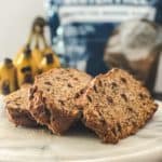 Chocolate chip banana bread slices on a white plate with banana bread in the background.