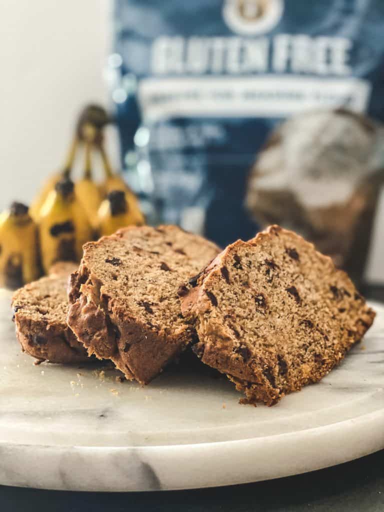 Chocolate chip banana bread slices on a white plate with banana bread in the background.