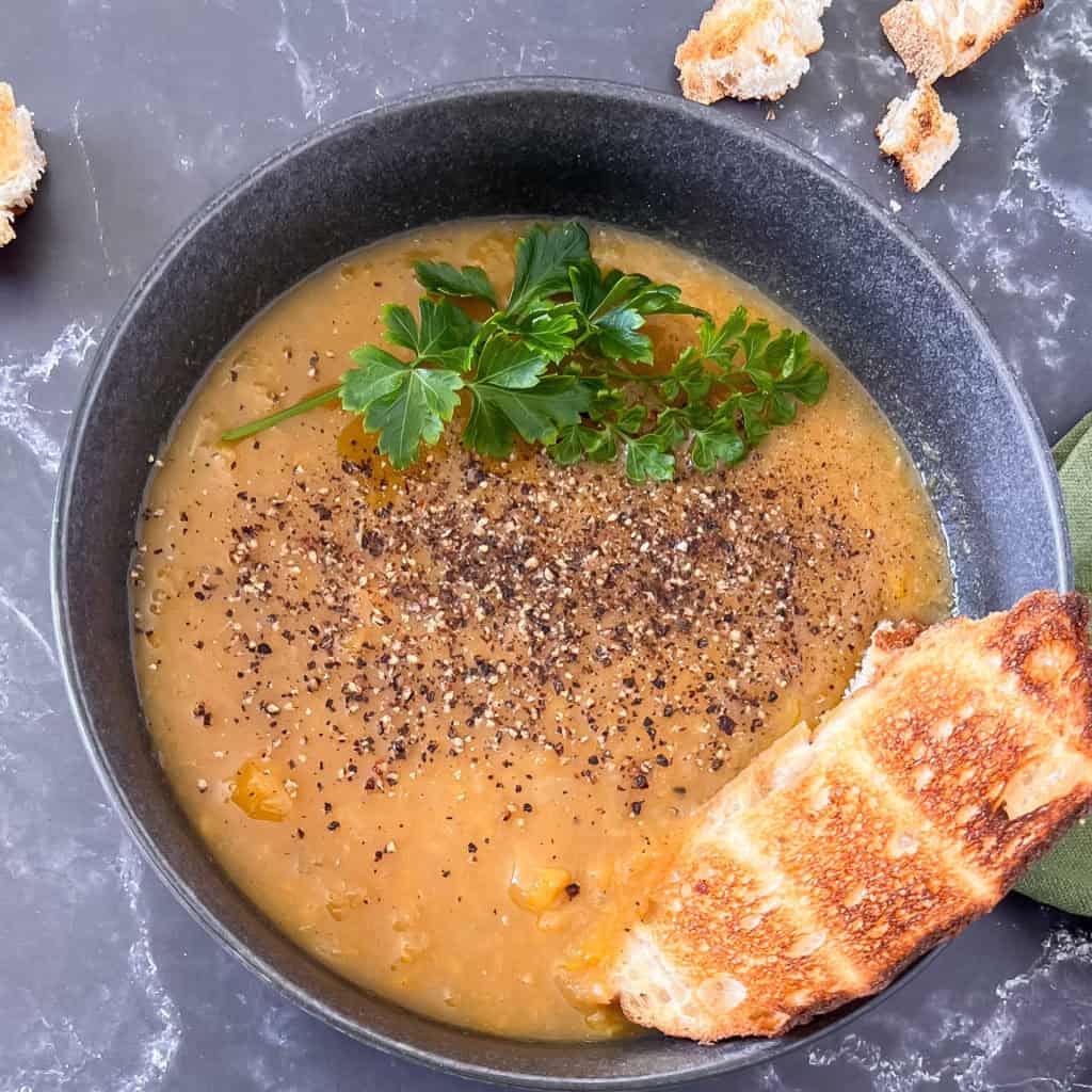 Apple and butternut squash soup with fresh pepper and parsley on top and a slice of toasted bread