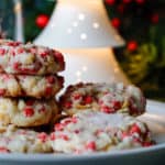 Festive shortbread base cookies with bright red cherry chips on a plate with holiday decor in the background
