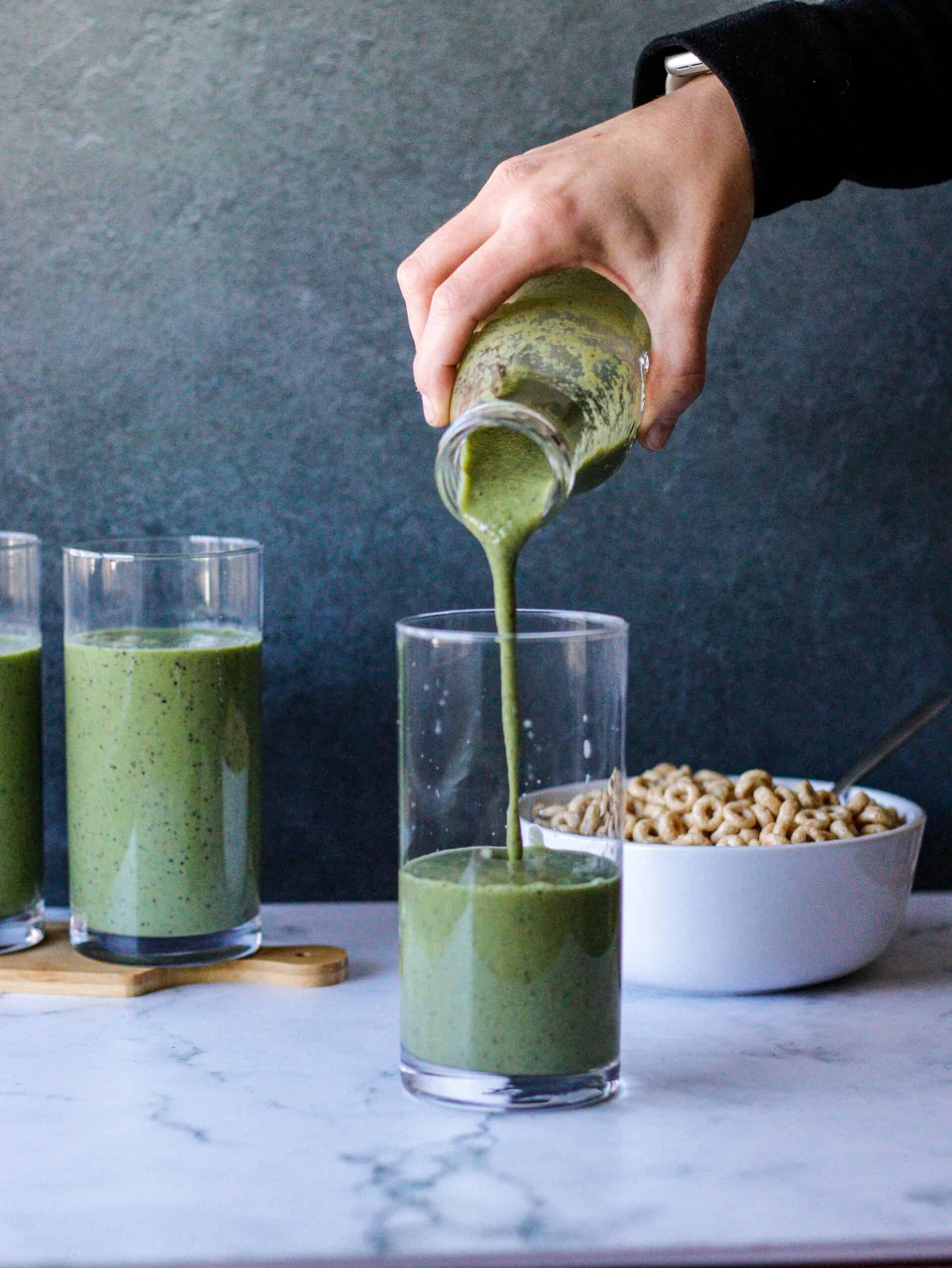 A vibrant green smoothie being poured into a clear glass, showcasing a nutritious blend of leafy greens, fruits, and wholesome ingredients for a refreshing and energizing beverage