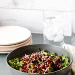 A gray bowl of bright green salad mix with red pomegranates and a dark balsamic glazed overtop
