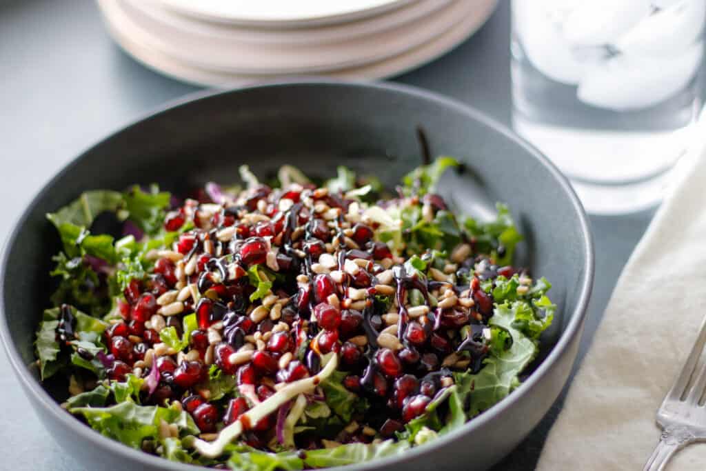 Bright greens and pomegranates with a balsamic drizzle in a gray bowl close up