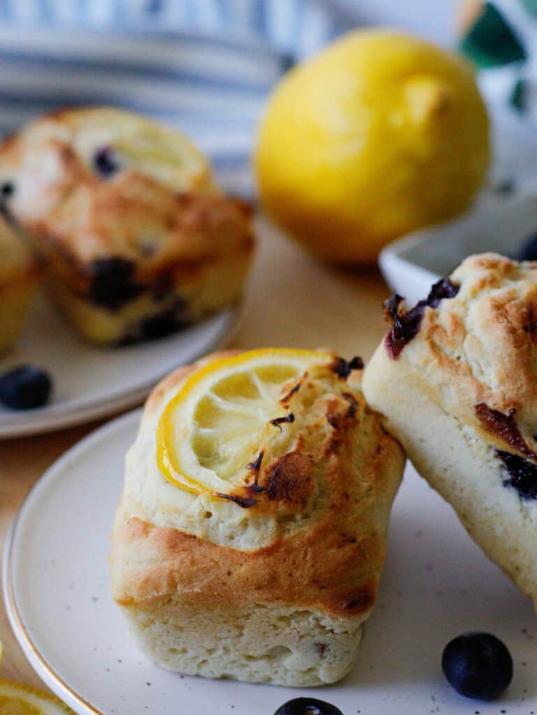 Mini lemon blueberry loaves on a plate with lemons in the background and blueberries scattered on the table