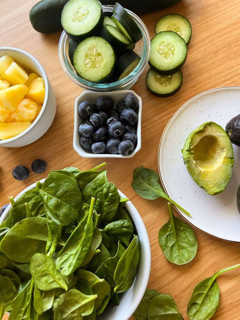 Ingredients laid out on table, spinach, pineapple, blueberries, cucumber and avocado