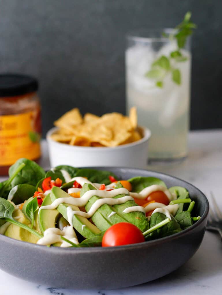 salad in a bowl with avocado on top and chips and salsa in the background 