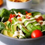 Salad in a bowl with avocado on top and chips and salsa in the background.