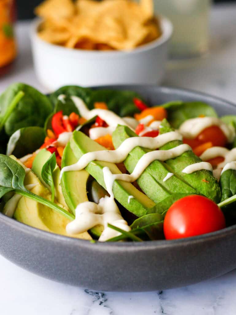 Salad in a bowl with avocado on top and chips and salsa in the background.