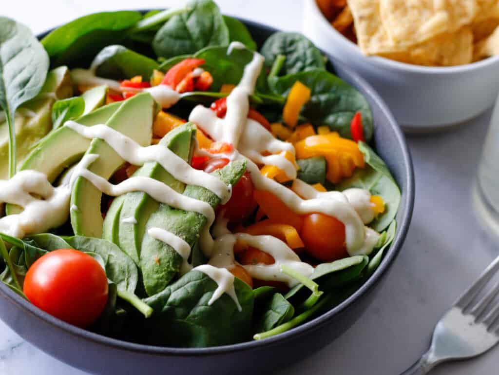 salad in a bowl with avocado on tip and white dressing drizzle 