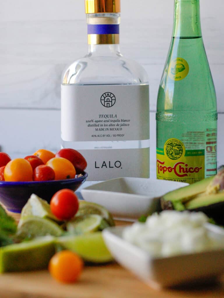 Two bottles in the background with cherry tomatoes and a cutting board in the foreground.