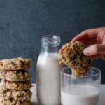 Stack of cookies with a hand dipping a cookie in a glass of milk