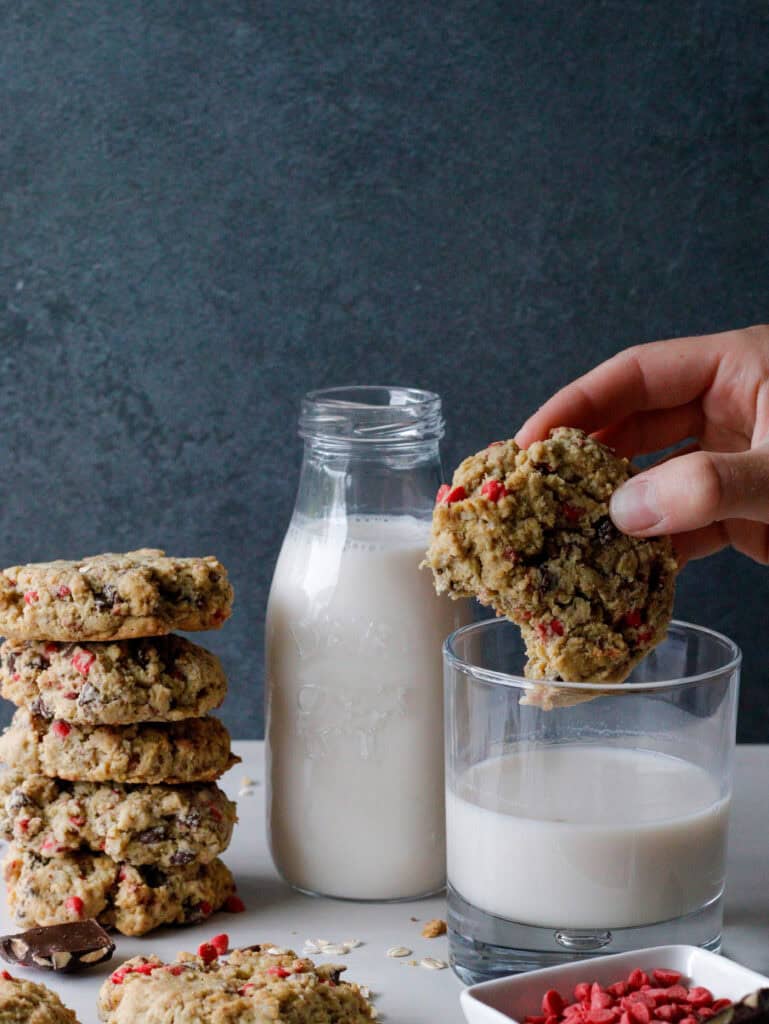 Cookies stacked with a glass of milk and a hand dunking the cooking in milk