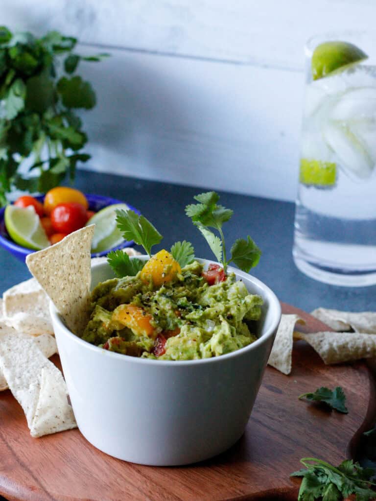 Bowl of guacamole with chips, cherry tomatoes and a glass of water in the background