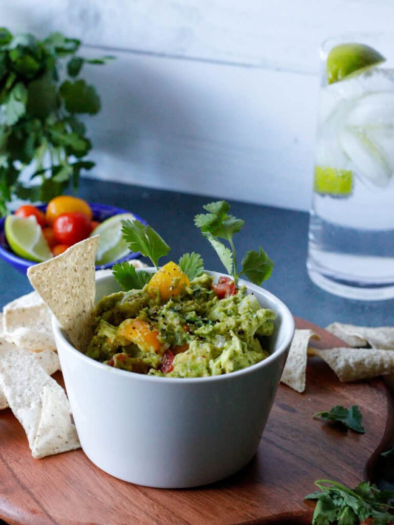 Bowl of guacamole with chips, cherry tomatoes and a glass of water in the background