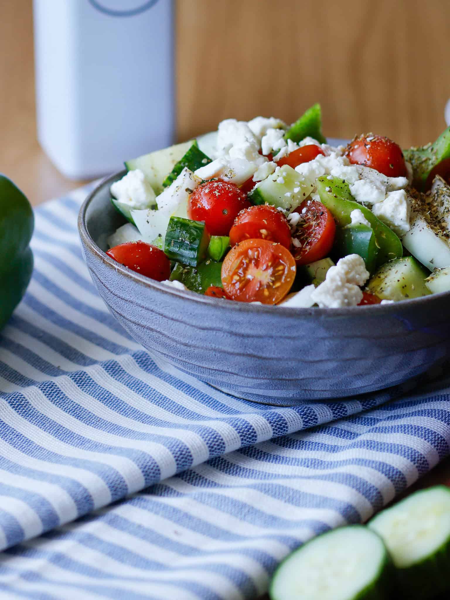 Bowl filled with tomatoes, feta cheese, cucumbers, green bell pepper on stripped napkin