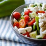 Bowl with tomato, cucumber, cheese, pepper with green bell pepper in background