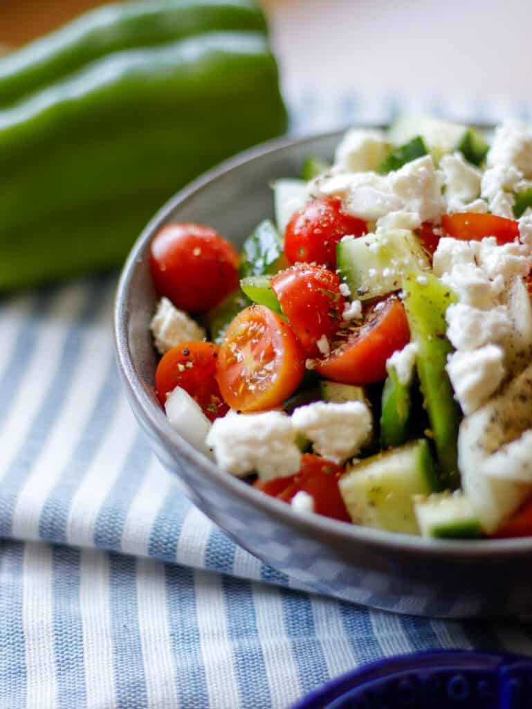 Bowl with tomato, cucumber, cheese, pepper with green bell pepper in background