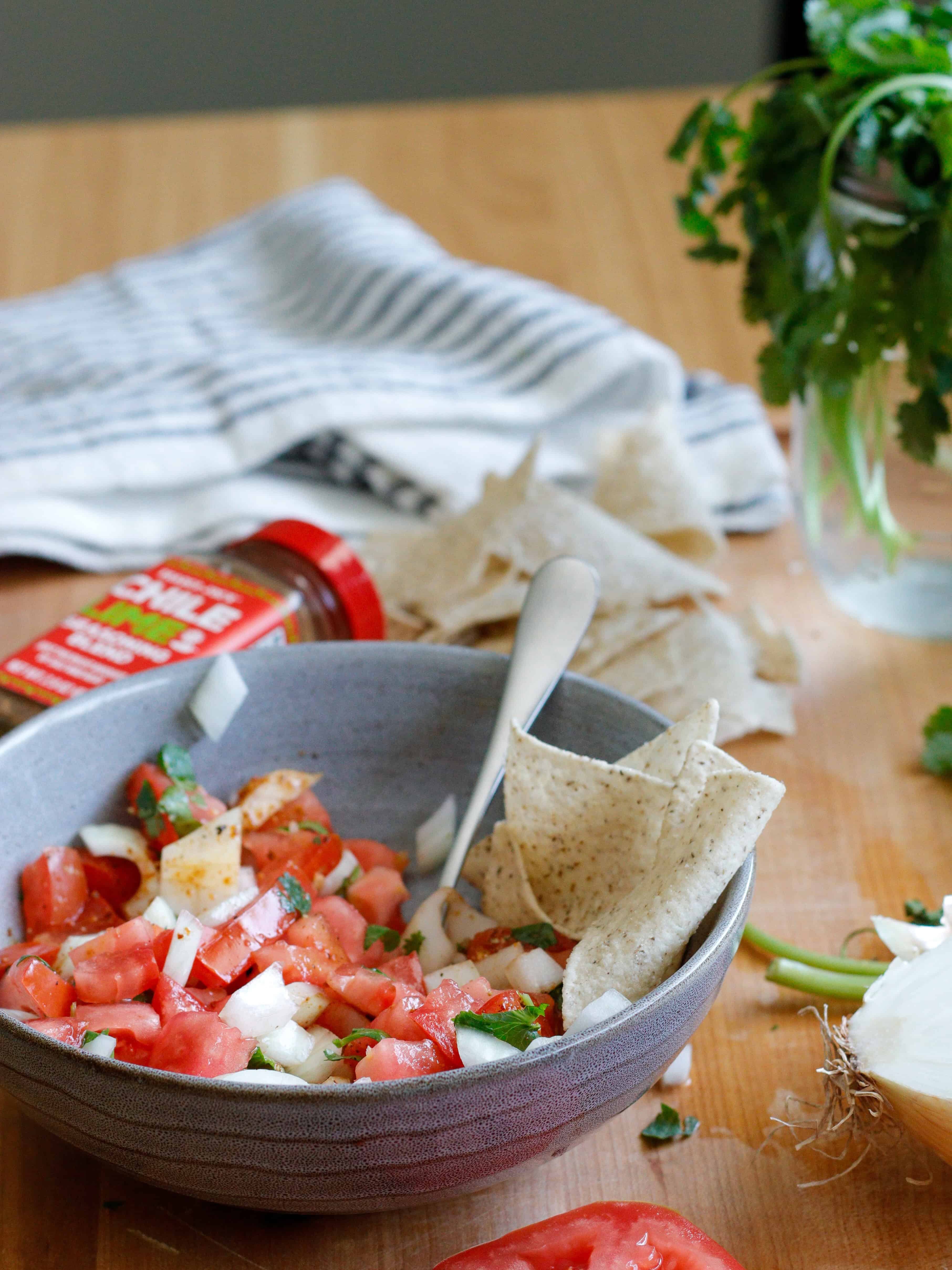 Gray bowl of pico de gallo with chips and cilantro in the background