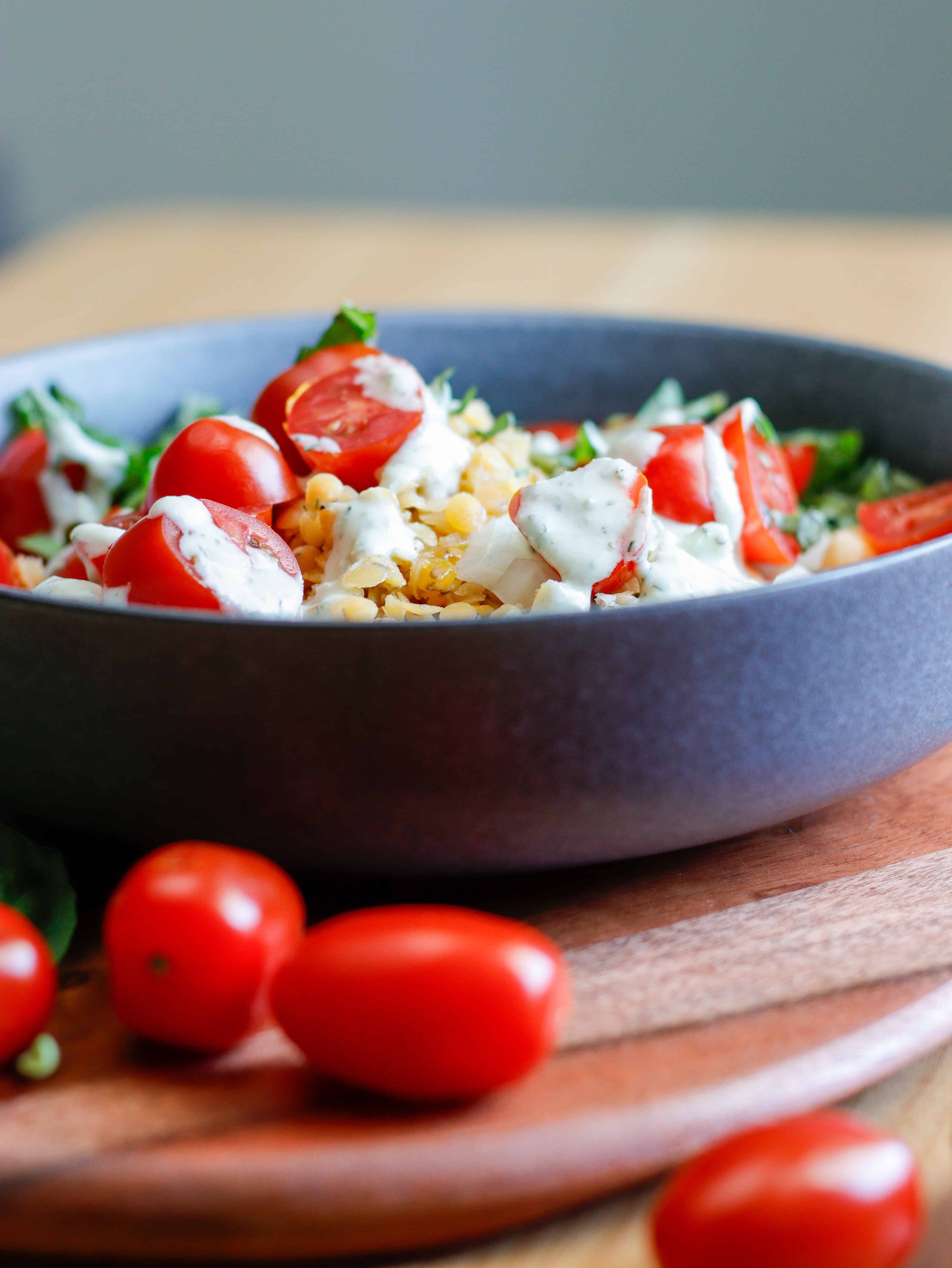 Bowl with tomatoes and lentils topped with a creamy dressing with cherry tomatoes in the foreground.