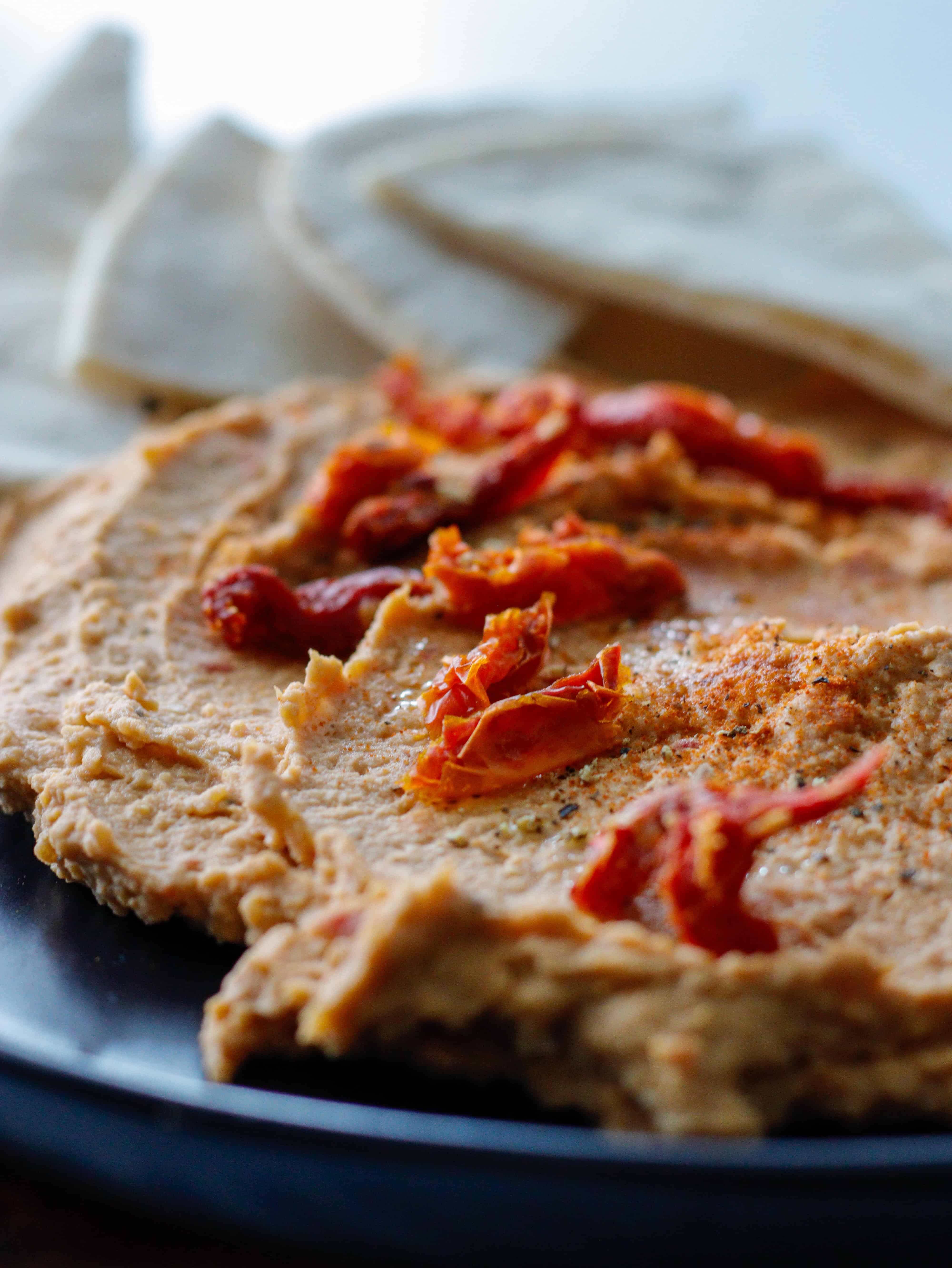 Sun-dried tomato hummus on a black plate close up with pita bread in the background.