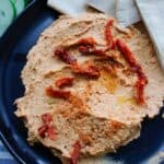 Overhead picture of hummus on black plate with pita bread and cucumber