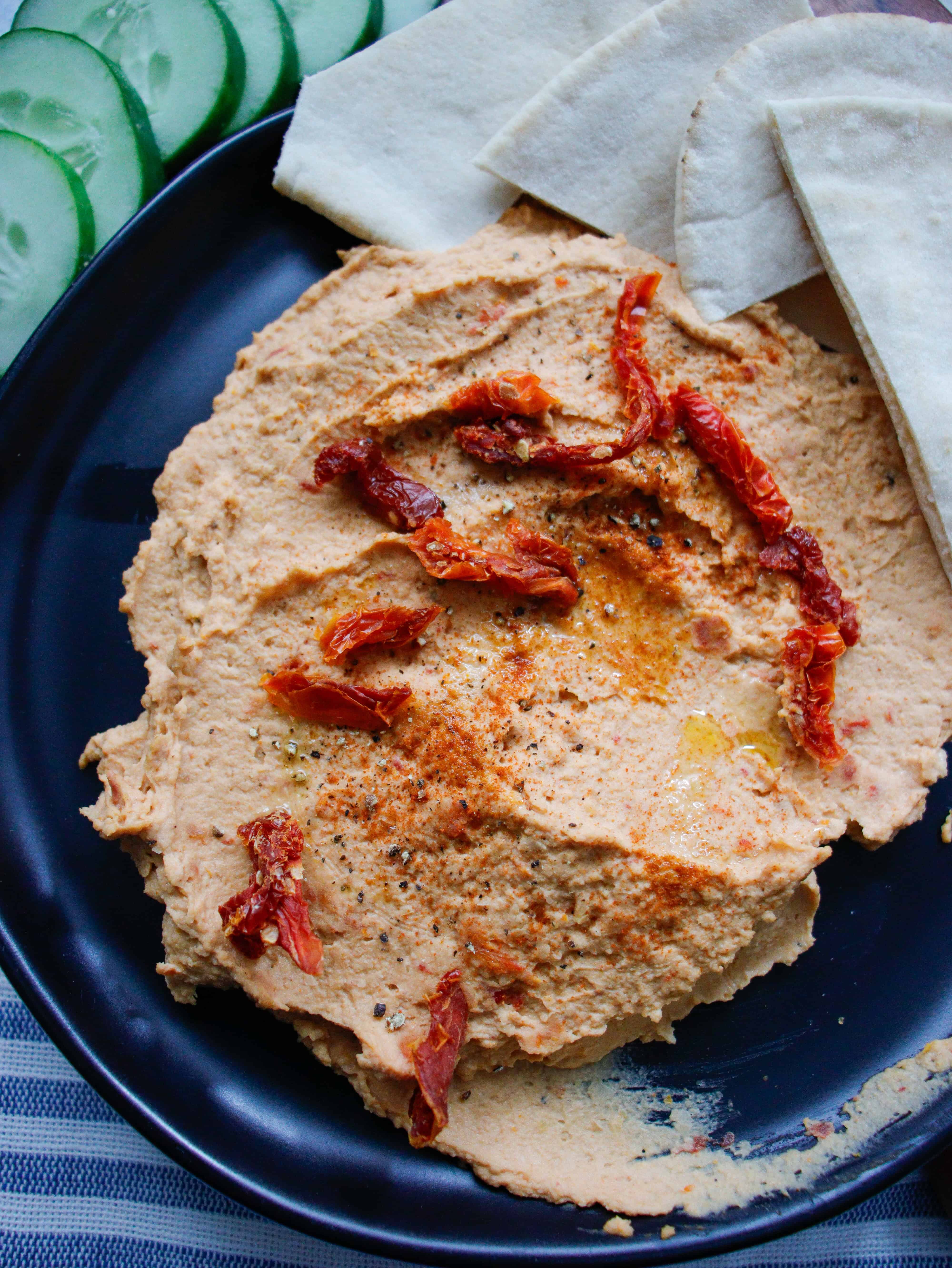 Overhead picture of hummus on black plate with pita bread and cucumber