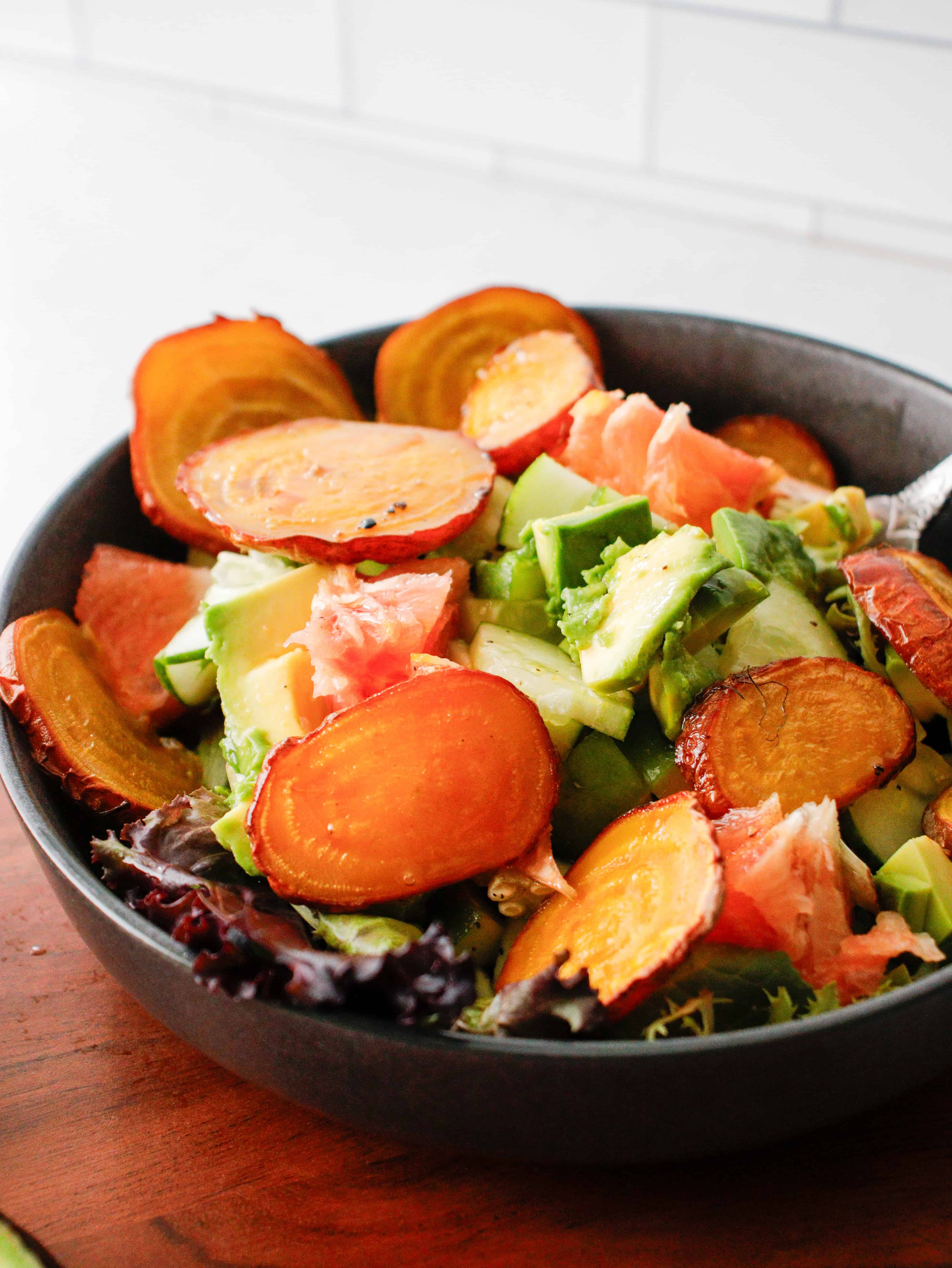 Salad with golden beets, avocado and grapefruit in a gray bowl on a wood counter.