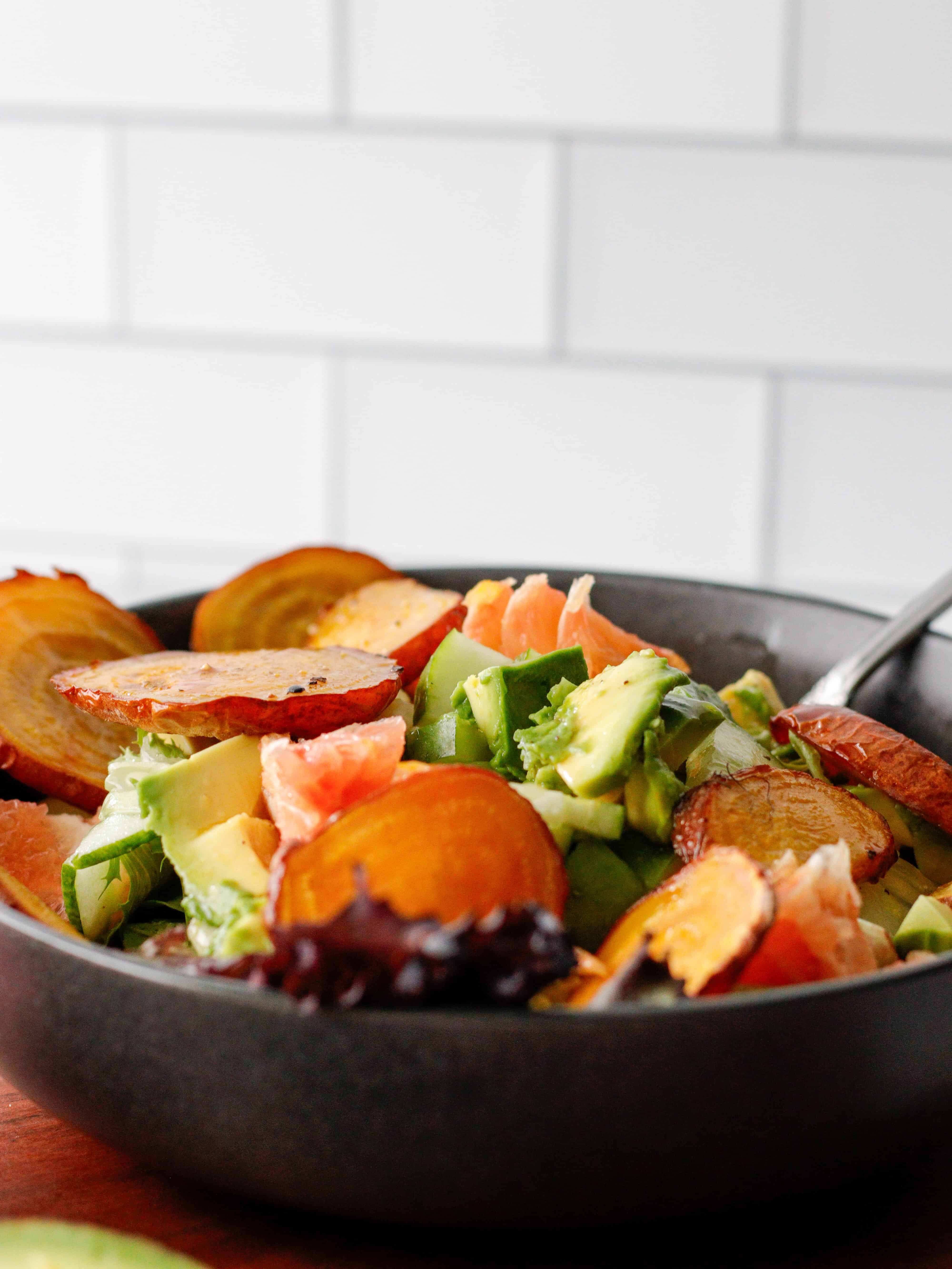 Salad with golden beets, avocado and grapefruit in a gray bowl on a wood counter.