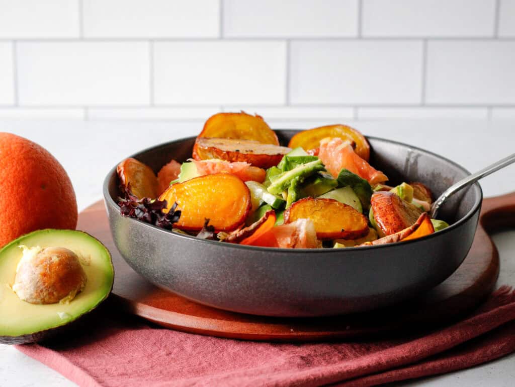 Salad with golden beets, avocado and grapefruit in a gray bowl on a wood counter.