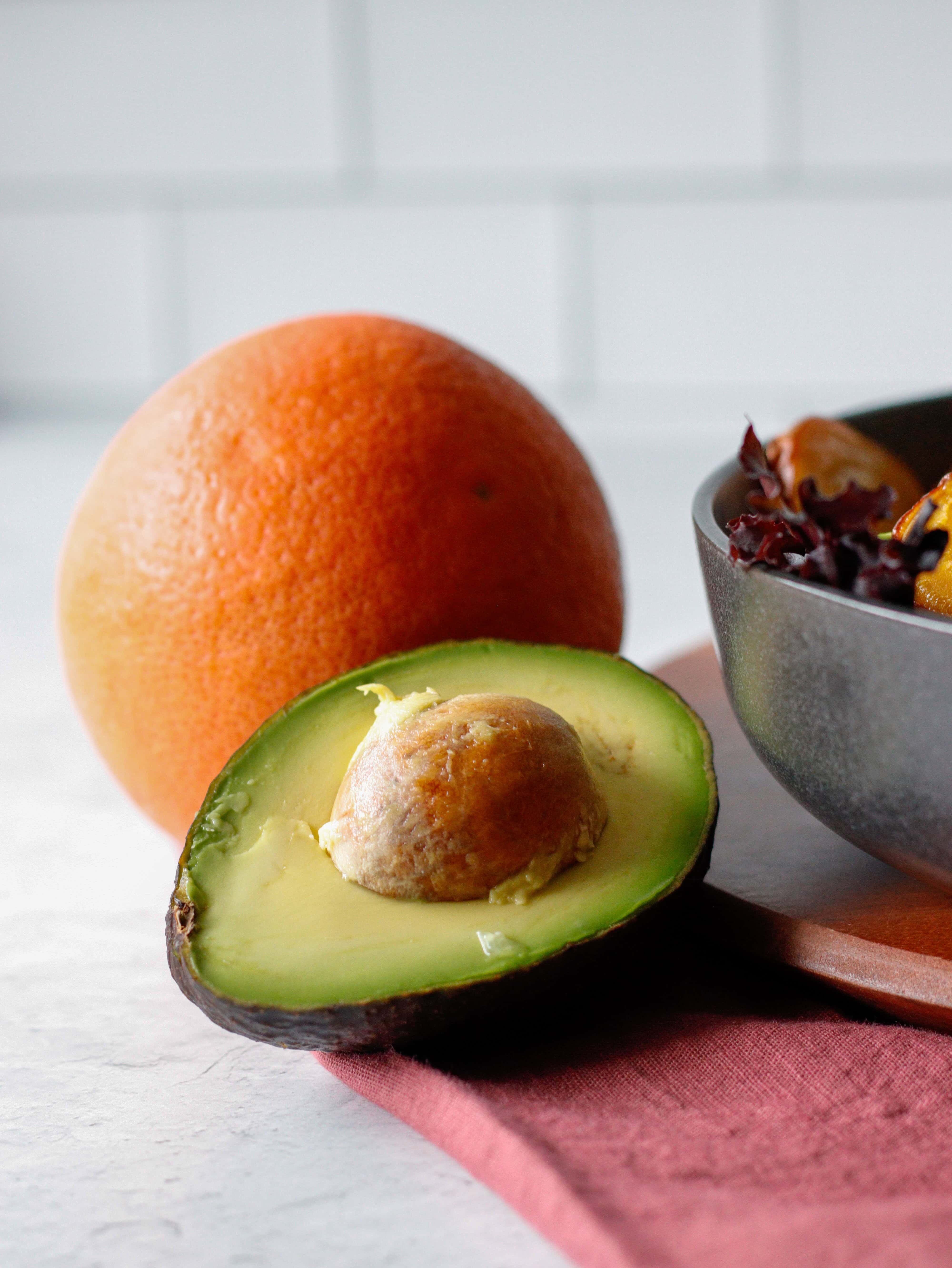 Fresh ripe avocado half with seed, whole grapefruit, and a bowl of colorful salad on a wooden tray, healthy and vibrant food ingredients, ideal for nutritious recipes and food photography.