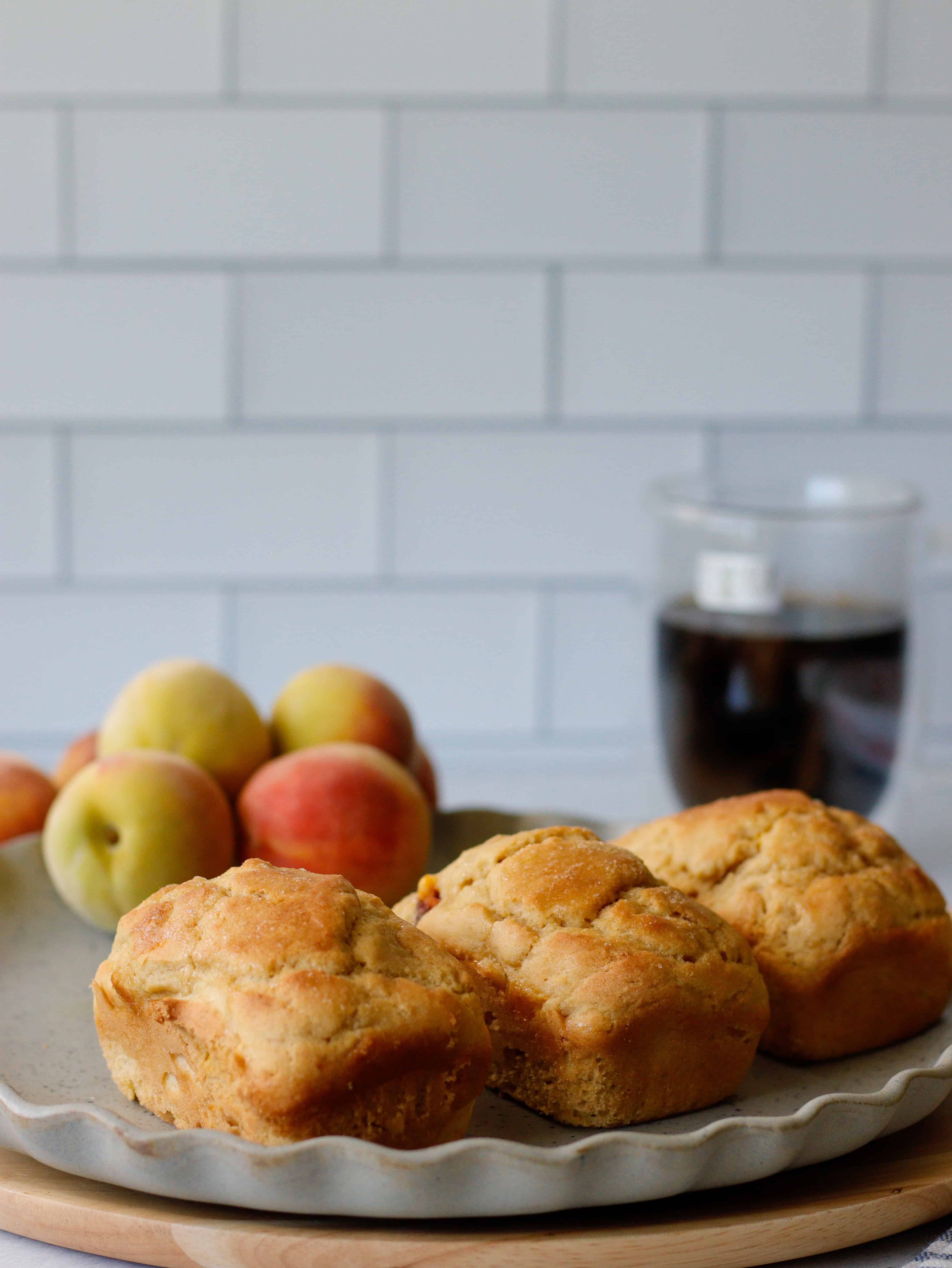 Mini peach loaves on a gray plate with peaches and coffee in the background.