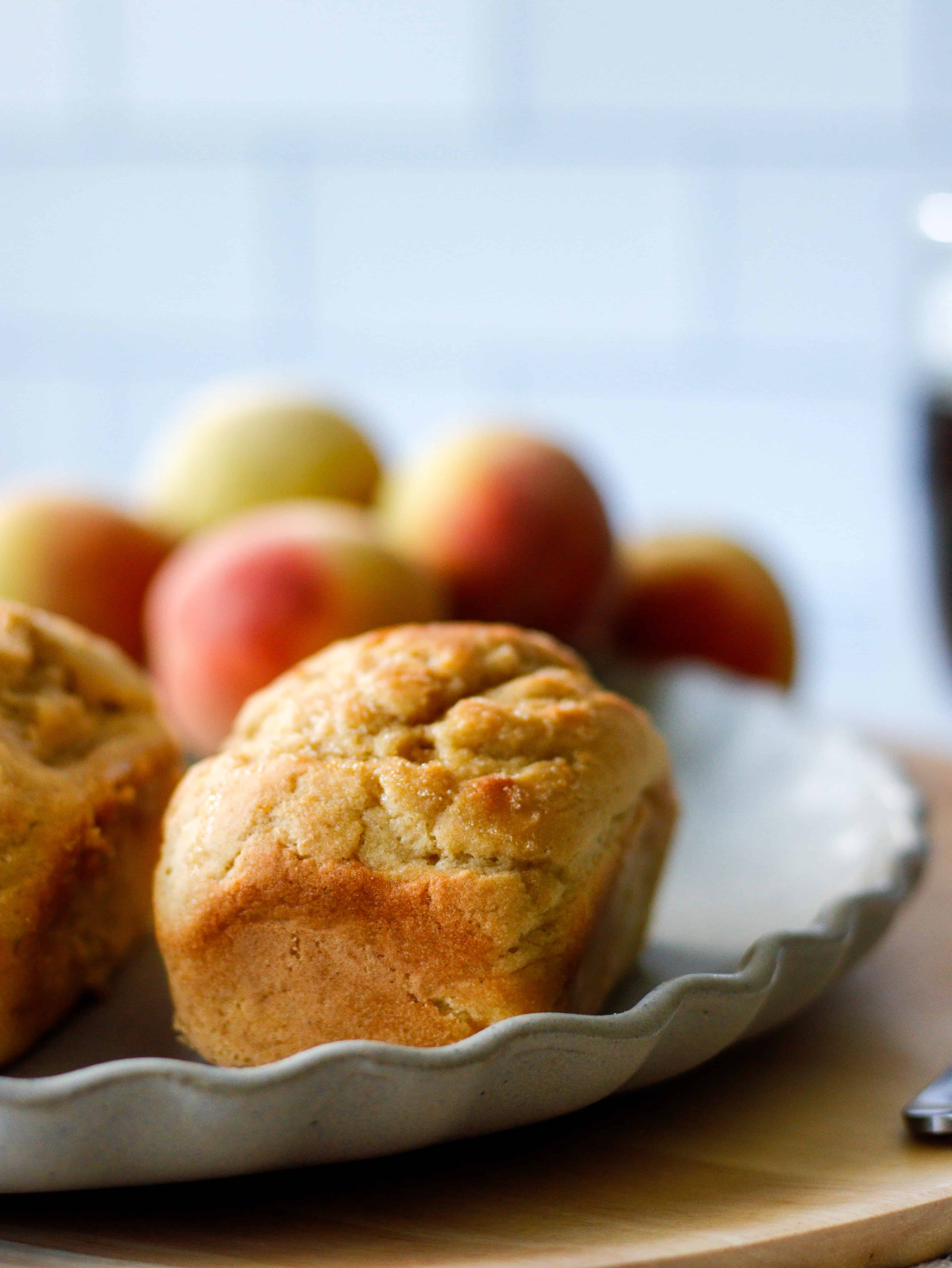 Single mini peach loaf of a gray plate with peaches in the background.