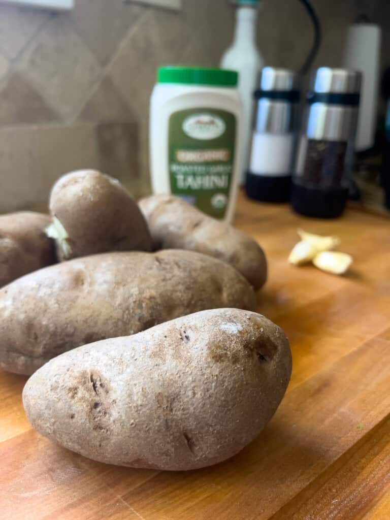 White potatoes on a cutting board with garlic and tahini in the background.