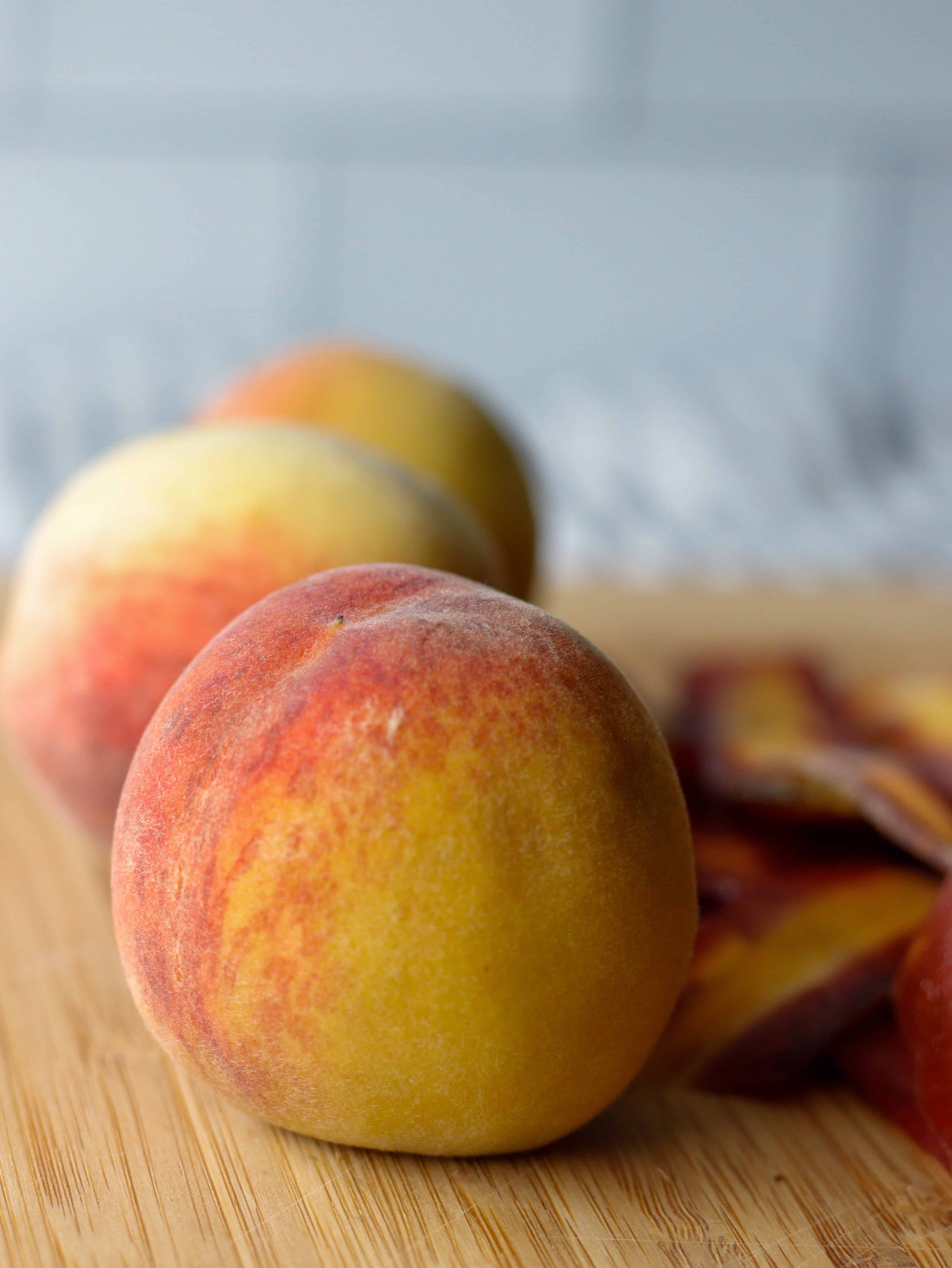 Three small peaches in a row on a cutting board ready to be cut for a salad