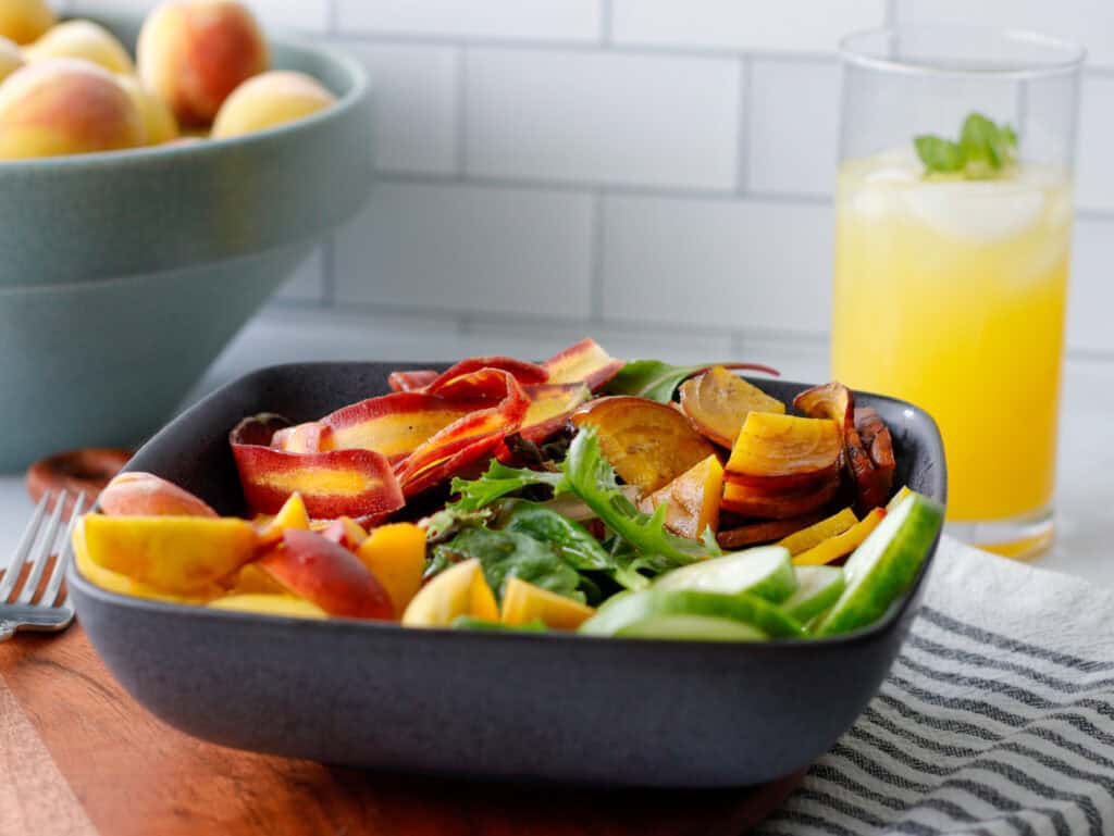 Peach salad in a bowl with peaches in the background and an orange drink in a glass.
