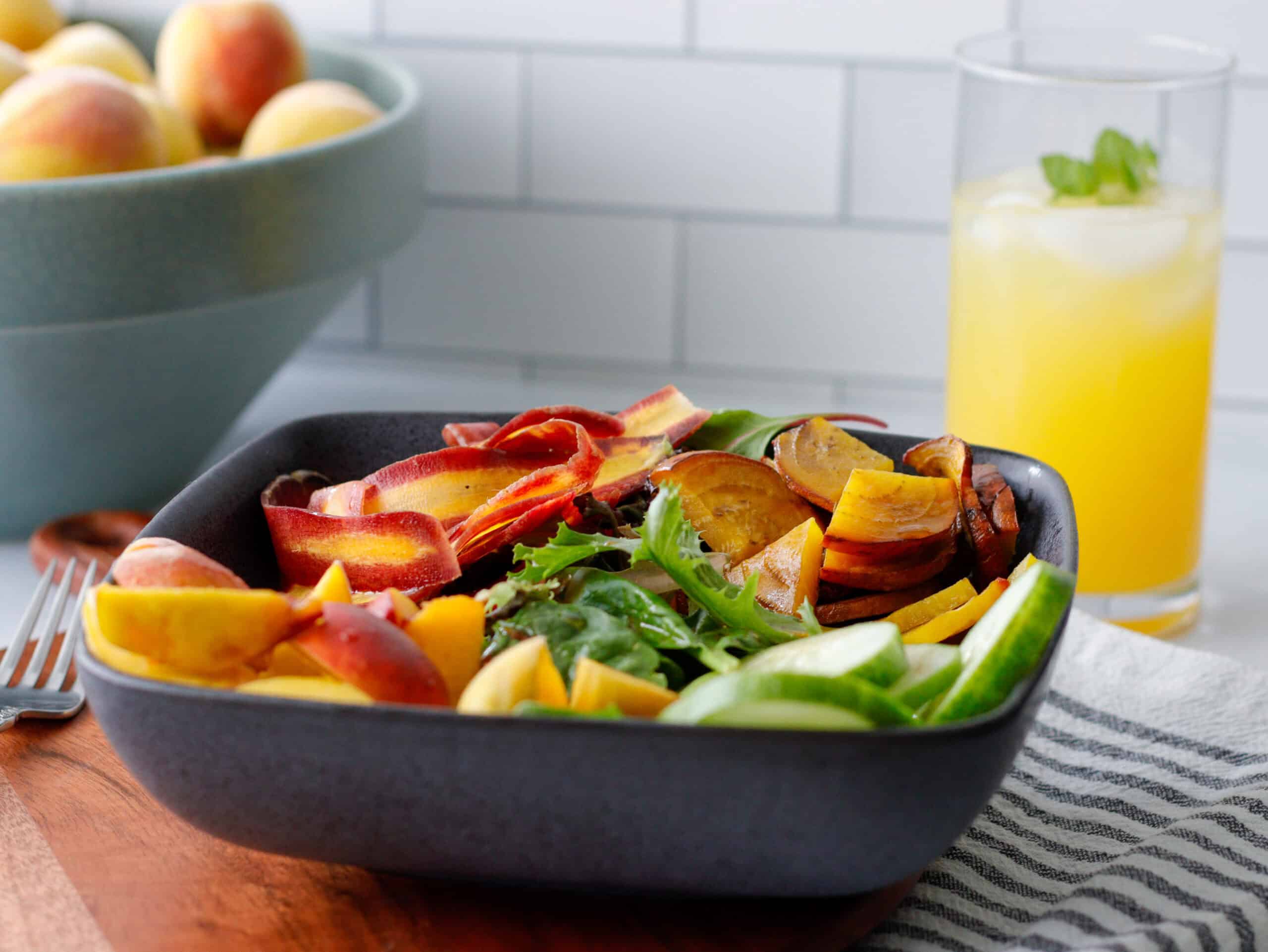 Peach salad in a bowl with peaches in the background and an orange drink in a glass.