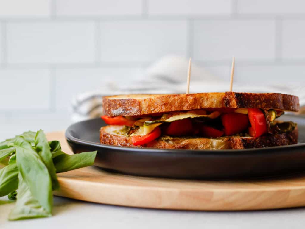 Sandwich on a black plate with pesto leaves on the side