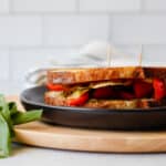 Sandwich on a black plate with pesto leaves on the side