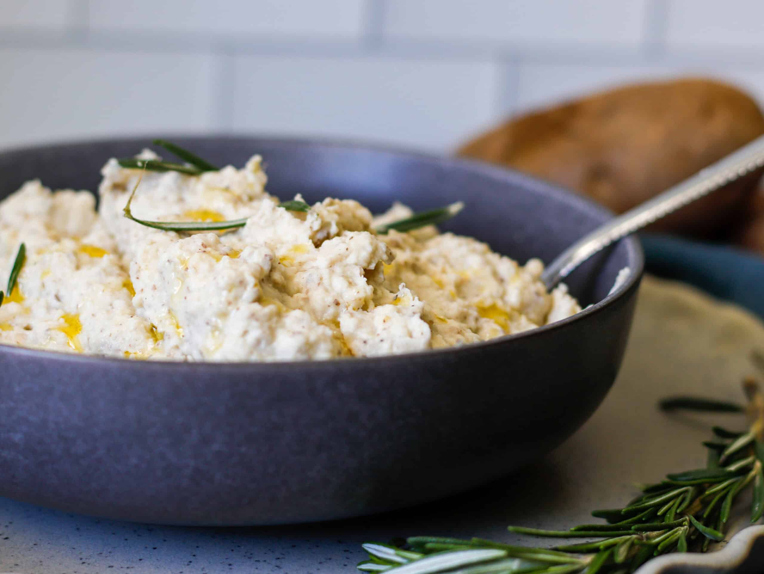 Mashed potatoes in a gray bowl with rosemary sprigs on top.