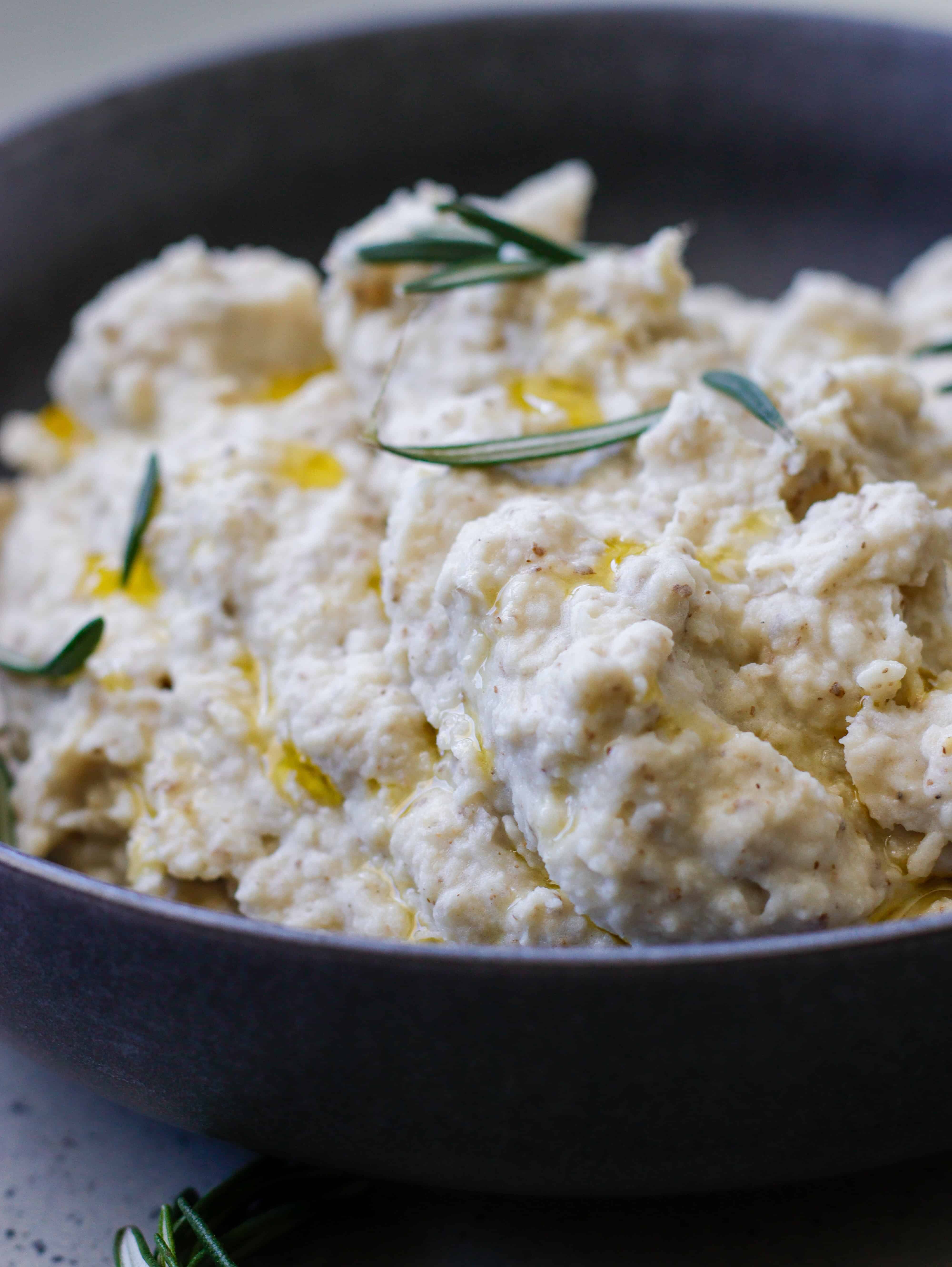 Mashed potatoes in a bowl with rosemary garnish.