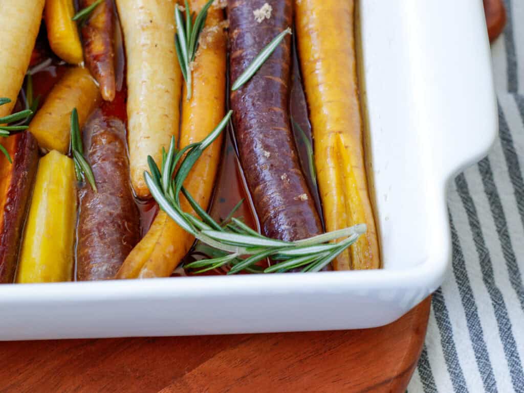 Rainbow carrots in a baking dish with rosemary sprigs on top