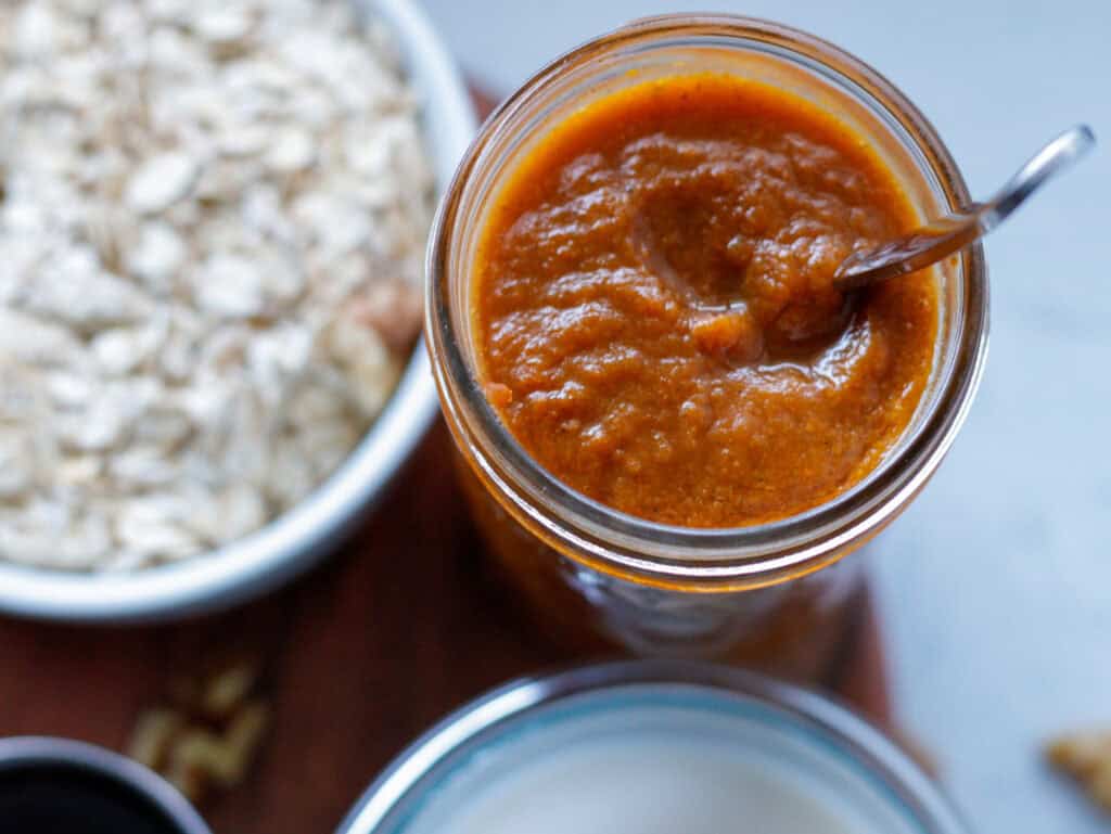 Pumpkin butter in a jar next to a bowl of oats