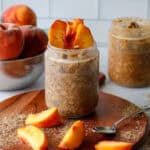 Peach overnight oats in a glass jar with peaches in the background and spread on the table