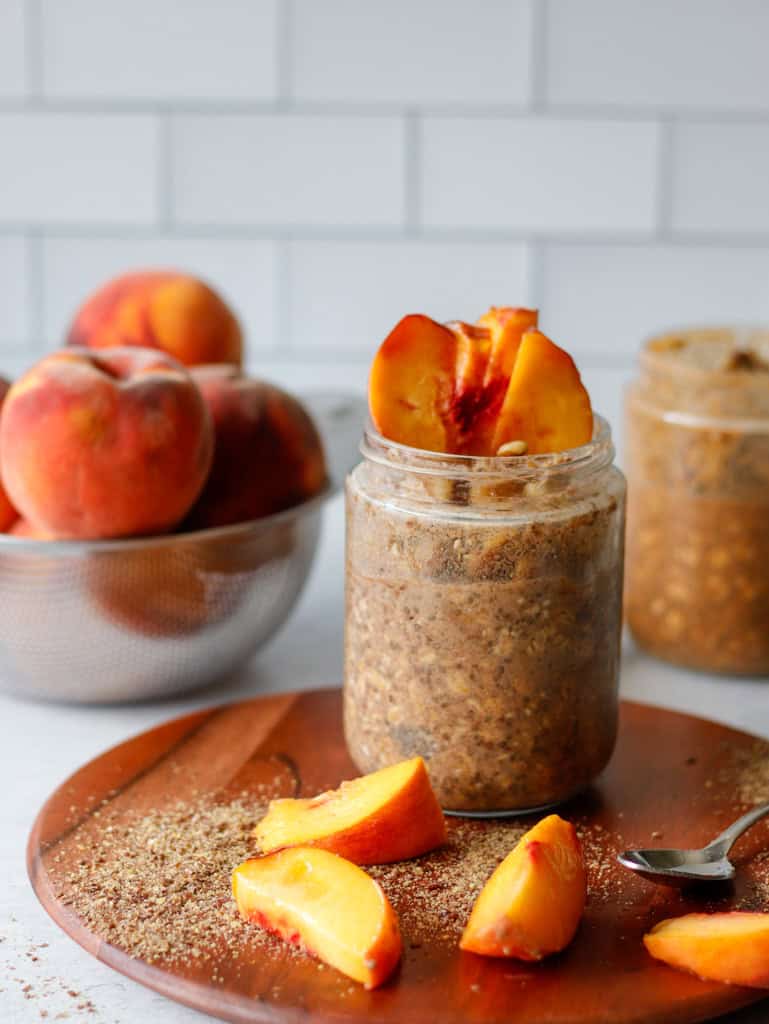 Peach overnight oats in a glass jar with peaches in the background and spread on the table